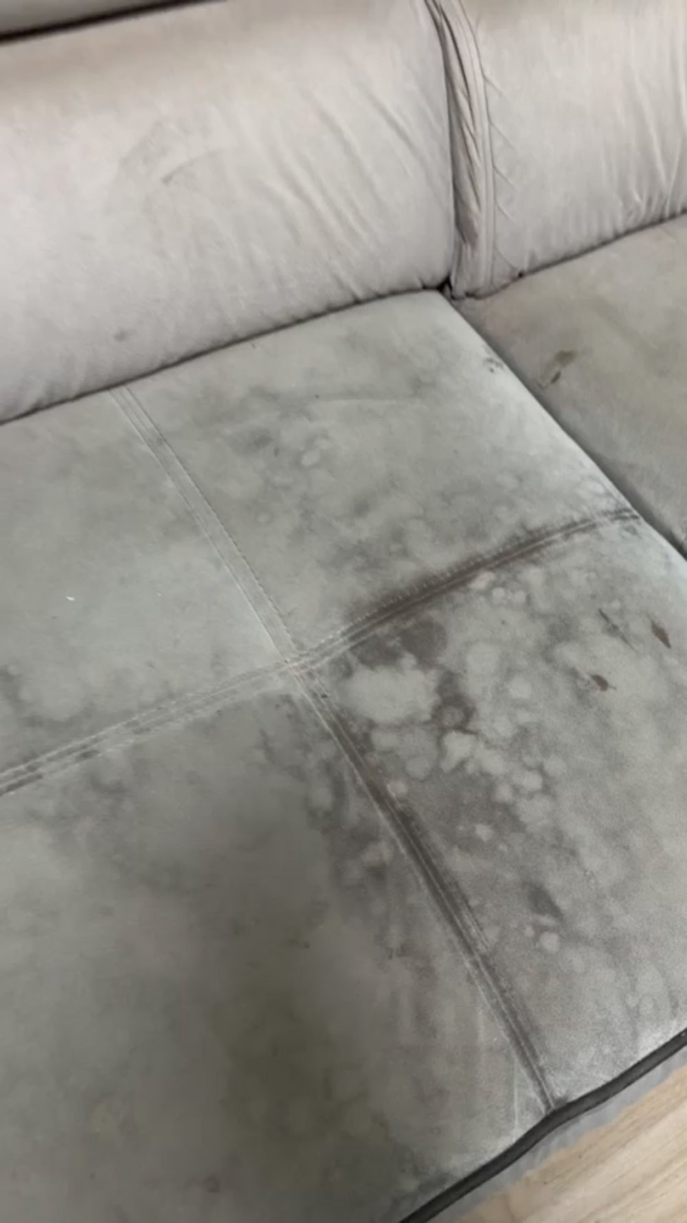 Assise de canapé en microfibre grise vue de près : saleté incrustée et auréoles sombres sur tout le coussin
