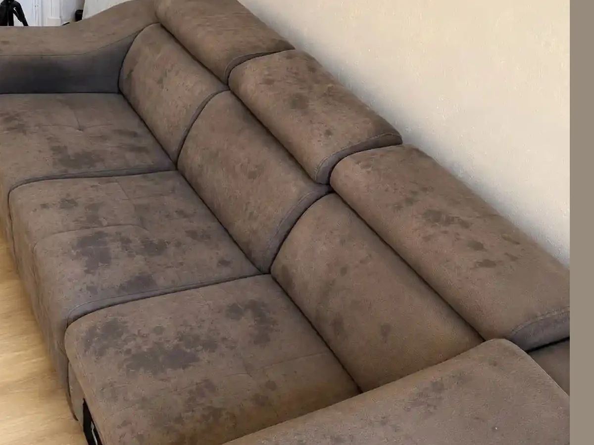 Canapé d'angle en tissu microfibre taupe avant nettoyage : taches sombres étendues sur l'assise, le dossier et les accoudoirs